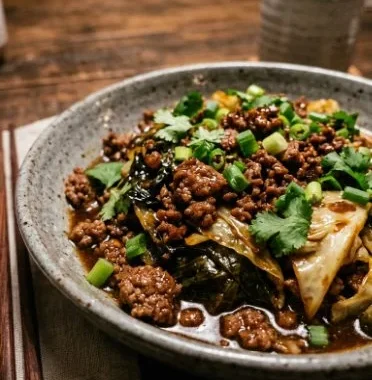 Plate of Mongolian ground beef cabbage stir-fry with green onions and sesame seeds.