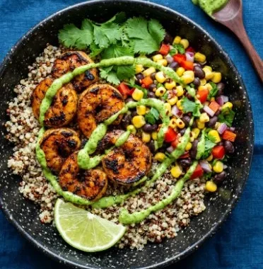 Chili lime shrimp quinoa bowl with colorful vegetables and lime garnish