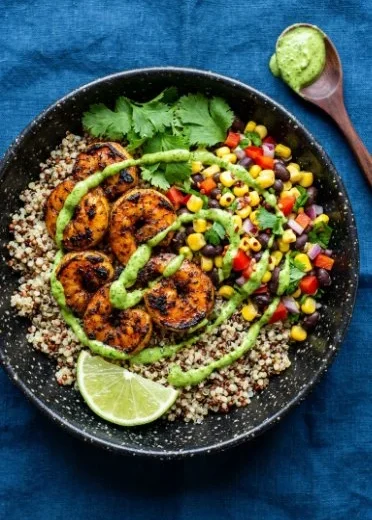 Chili lime shrimp quinoa bowl with colorful vegetables and lime garnish