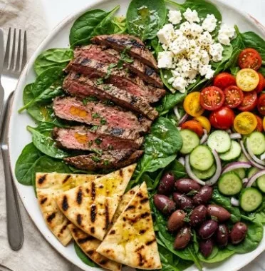 A colorful grilled steak salad topped with fresh vegetables and a tangy dressing.