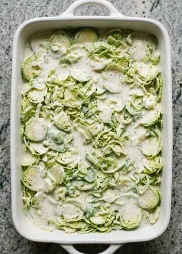 Baked Brussels Sprouts Gratin topped with cheese in a white dish