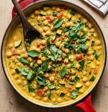 Chickpea satay casserole topped with creamy sauce and fresh herbs.