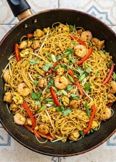 Plate of Singapore Noodles with Chicken and Shrimp garnished with vegetables