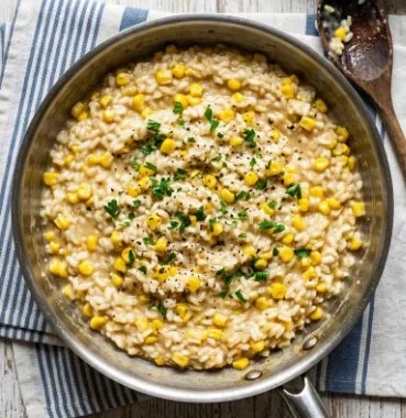 Bowl of creamy Sweet Corn Risotto garnished with fresh herbs and corn kernels.