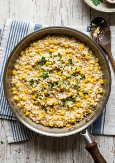 Bowl of creamy Sweet Corn Risotto garnished with fresh herbs and corn kernels.