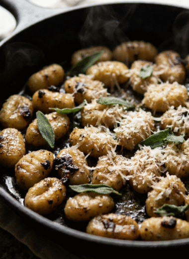 Black garlic gnocchi in a cast-iron skillet topped with Parmesan and fresh sage
