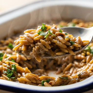 Black Garlic Orzo: A Modern Umami Twist 9 Spoon lifting creamy black garlic orzo from a baking dish, garnished with parsley and pine nuts
