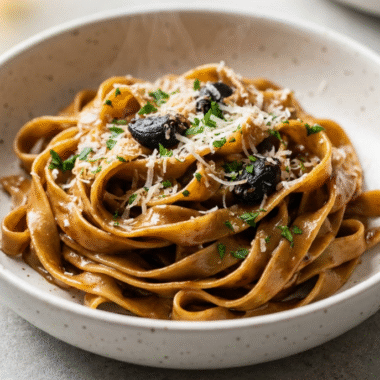 Black garlic fettuccine in a white speckled bowl topped with Parmesan and parsley