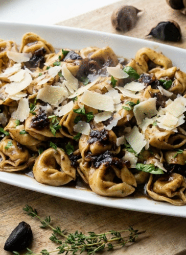 Black garlic tortellini in a rich caramelized black garlic sauce, topped with shaved Parmesan and fresh herbs, served on a white platter